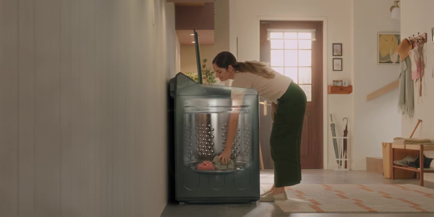 Máy giặt cửa trên màu đen với lồng giặt inox, người dùng đang cho quần áo vào máy